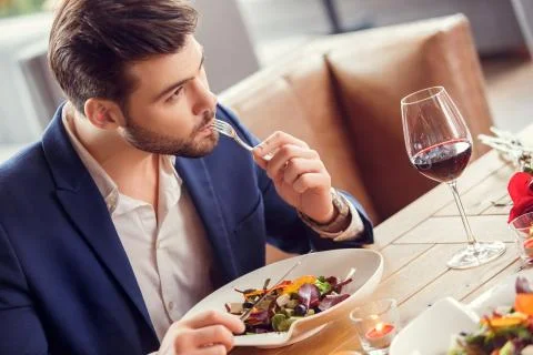 Young man close-up on date in restaurant sitting eating salad thoughtful Stock Photos