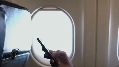 Young man in close-up is using a smartphone inside an airplane next to a window. Stock Footage 98293600