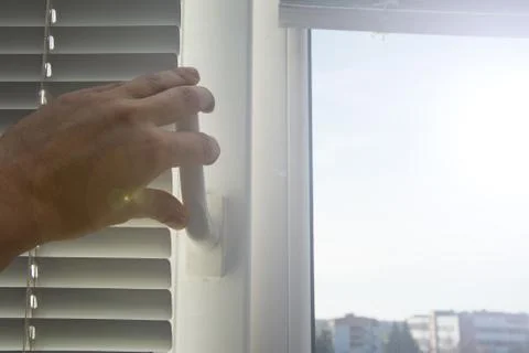 A young man closes or opens window with lowered horizontal white aluminum bli Foto stock