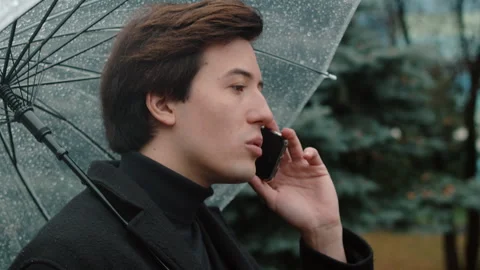 Young man in a coat close up walking under a transparent umbrella in the autumn Video stock 257402204