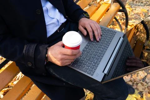 Young man with coffe and using laptop in the autumn park, top view. Stock Photos