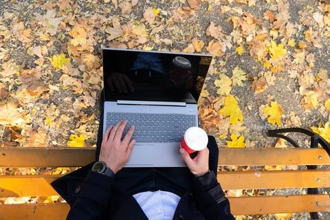 Young man with coffe and using laptop in the autumn park, top view. Foto stock