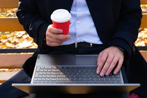 Young man with coffe and using laptop in the autumn park, top view. Stock Photos