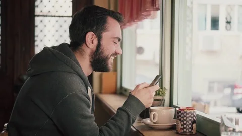 Young man at coffee shop texting on his phone Stock Footage 72473594
