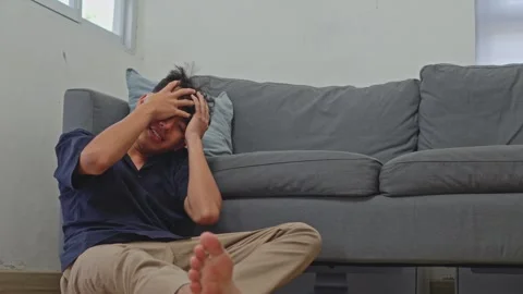 Young man collapses holding head in pain from vertigo onto living room floor by Stock Footage 335892035