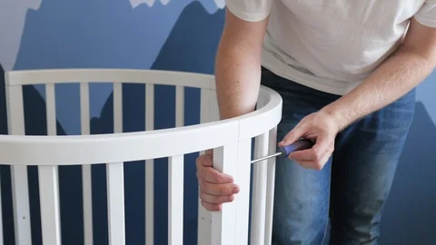 Young man collects a crib with a screwdriver for an unborn child. man collects a Stock Footage 118631853