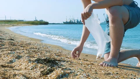 A young man collects shells in a plastic bag on the beach. Stock Footage 96127476