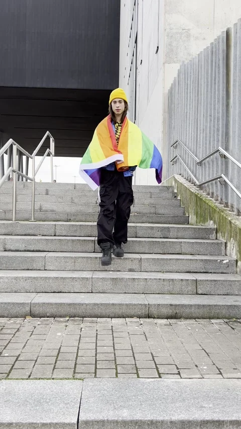 Young man in colorful clothes walking down a ladder with the pride flag Stock Footage 259853315