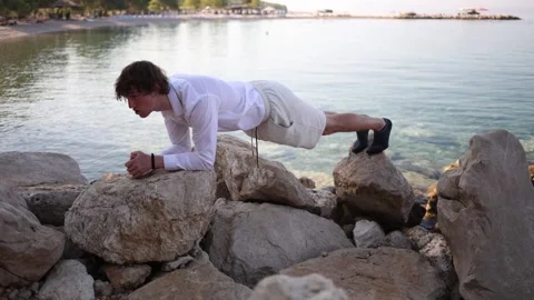 Young man combines seaside vacation with fitness training on coastal rocks 库存影片 341622883
