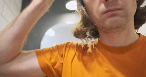 Young man combing his long shaggy hair with comb. Bathroom, mirror. Problematic Stock Footage 255795678