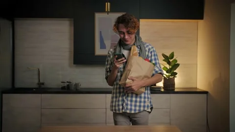 Young Man come home from store carrying paper bag with food in kitchen.Checking Stock Footage 221619388