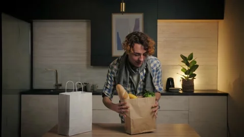 Young Man come home from store carrying paper bag with food in kitchen.Checking Stock Footage 221619631