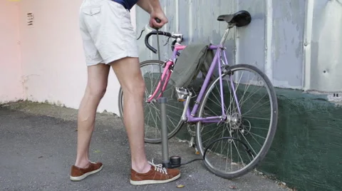 Young man comes to pump up the wheel in the bike Stock Footage 65316857