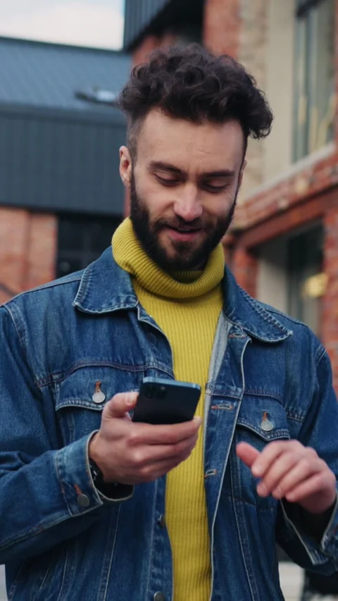 A young man comfortably using his smartphone while sitting outdoors in an urban Stock Footage 314209885