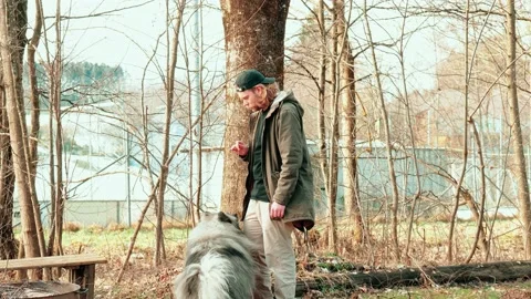 This young man commands his fluffy gray dog to sit down. The wolfspitz Stockbeeldmateriaal 234444818