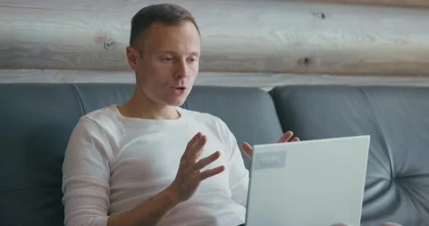 Young man communicates via video link using laptop while sitting on the couch Stock Footage 199317426