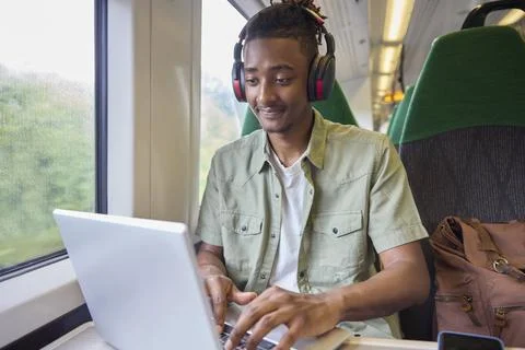Young Man Commuting To Work Sitting  On Train Working On Laptop Computer Foto stock