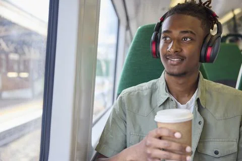 Young Man Commuting To Work Sitting  On Train Wearing Wireless Headphones W.. Stock Photos