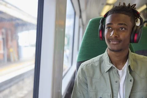 Young Man Commuting To Work Sitting  On Train Streaming Music Or Podcast To.. Stock Photos