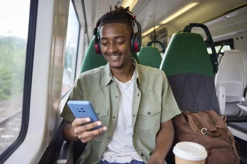 Young Man Commuting To Work On Train Sitting  On Train Looking At Mobile Ph.. Foto stock