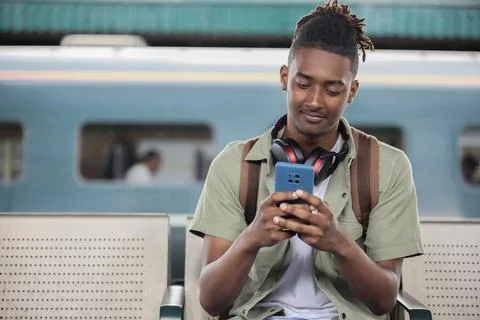 Young Man Commuting To Work On Train Sitting  On Platform Looking At Mobile.. Foto stock