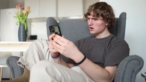 The young man is in complete bewilderment, staring at his phone in disbelief at  Stock Footage 302634327