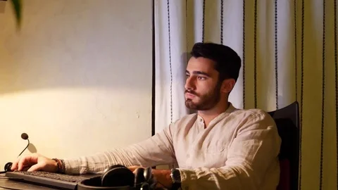 Young man at computer putting on headphones Stock Footage 81245596