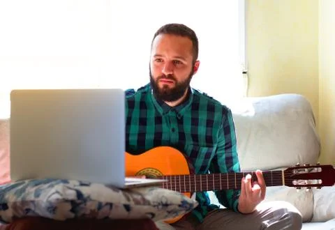 Young man concentrating as he learns to play the guitar thanks to a tutorial  Stock Photos