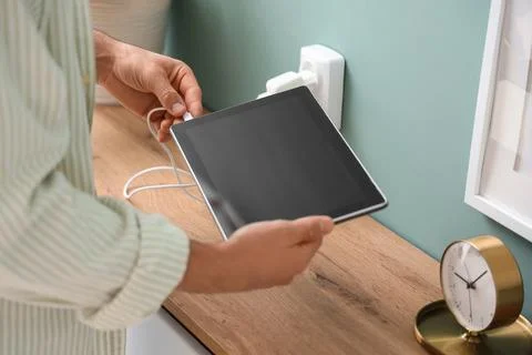 Young man connecting charging cable to tablet at home, closeup Stock Photos