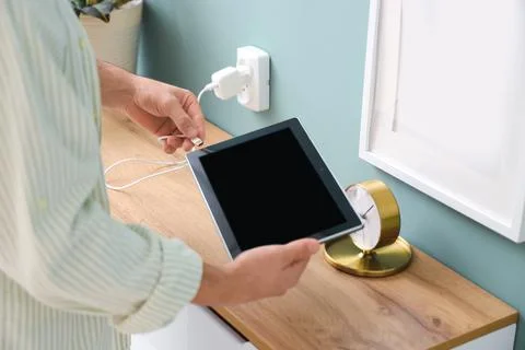 Young man connecting charging cable to tablet at home, closeup Stock Photos