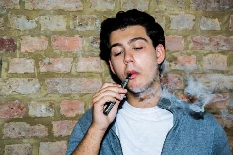 Young man contentedly puffing on an e-cigarette Stock Photos