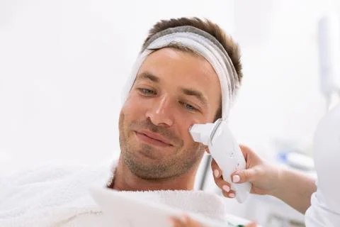 Young man control the condition of his skin in the beauty salon Stock Photos