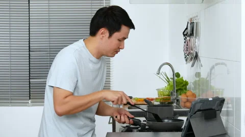 Young man cooking and preparing food according to a recipe on a tablet computer  Stock Footage 170711289