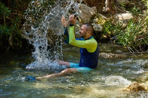 A young man cools off in the cold water of a mountain river on a hot summer d Stock-Fotos