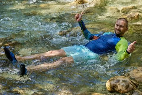 A young man cools off in the cold water of a mountain river on a hot summer d Stock Photos