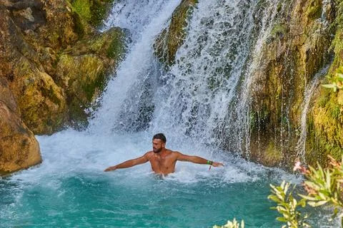 A young man cools off in the waterfall of a cold mountain river on a hot su.. Stock Photos