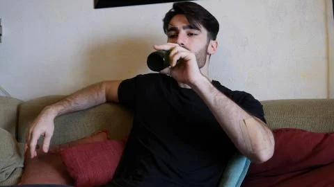 Young man on couch drinking beer Stock Photos