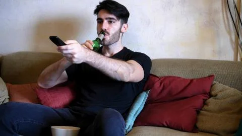 Young man on couch drinking beer and eating Stock Photos