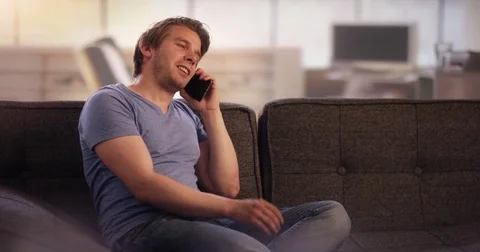 Young man on couch having a funny telephone call Stock Footage 78628384