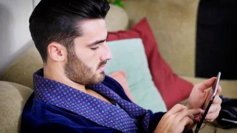Young man on couch reading with tablet PC Stock Photos