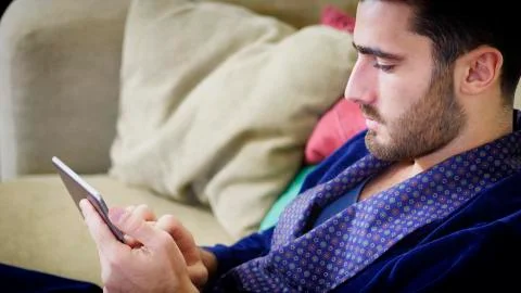 Young man on couch reading with tablet PC Stock Photos