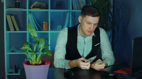 Young man counts money, sitting in armchair before computer in office Stock Footage 160446737
