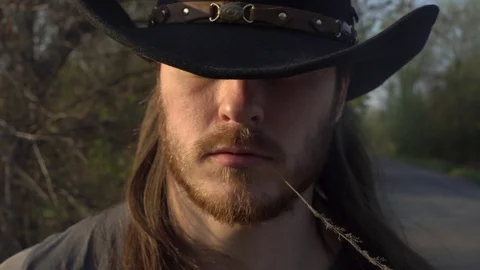 A young man, a cowboy, in a hat with a red beard and a straw in his mouth, walks Stock Footage 129571388