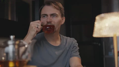 A young man in a cozy atmosphere drinks tea by the window of the house Stock Footage 294239865