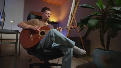Young man in creative authentic home interior plays acoustic guitar learning Stock Footage 315663513