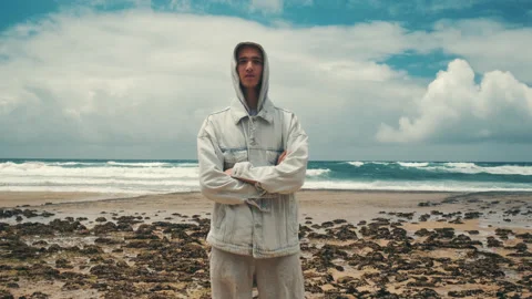 Young man with crossed hands is  posing against blue sea with clouds on the.. Stock Footage 254656853