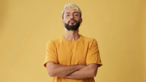 Young man crossing arms, looking at camera isolated on yellow background in Stock Footage 254914366