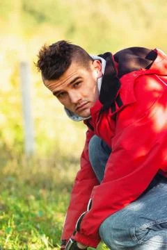 Young man crouching down in red jacket covered with beautiful shadow Stock Photos