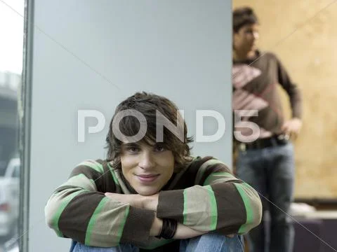 Young man crouching, portrait, other young man leaning in background Stock Photos