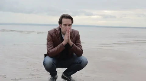 Young man crouching by the sea 스톡 동영상 53840300